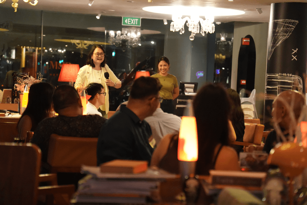 A host opens the evening for guests seated across the riverside restaurant.