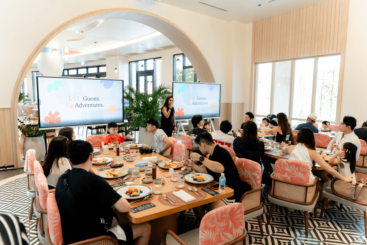 Families gather for the welcome lunch, Little Guests Big Adventures on the screens behind.